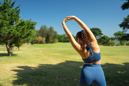 A woman stretching her arms backward in the park on a sunny day. Outdoor exercise.