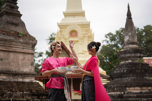 Young Thai couple wearing Thai costumes playing in the water during Songkran in the temple