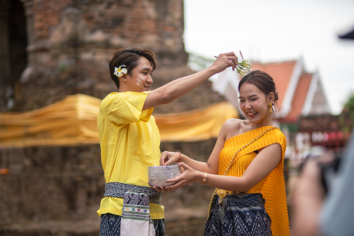 A beautiful Young Thai couple wearing Thai costumes playing in the water during Songkran in the temple