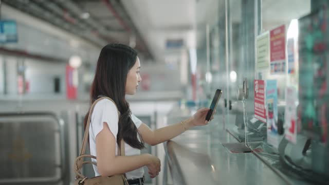 An Asian woman using a smartphone for contactless payment at the railway station