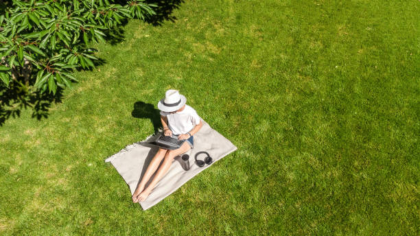 istock Young woman using laptop computer in park, student girl freelancer working and studying online outdoors sitting on grass with headphones and laptop, aerial drone view from above 1971955421