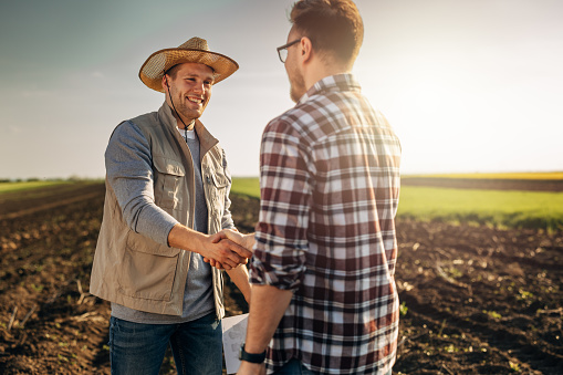 Happy farmer shakes hands with an owner of the farmland he just bought.
