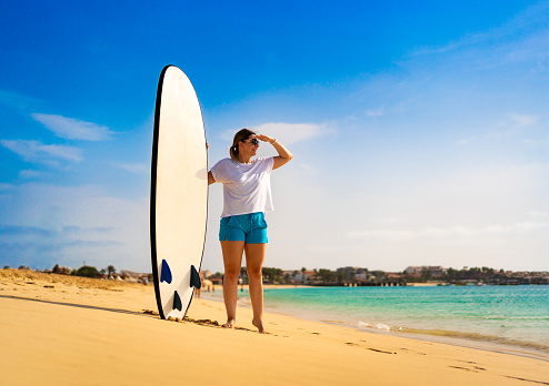 Beautiful woman holding surfboard standing on sunny beach Santa Maria, Sal island , Cape Verde