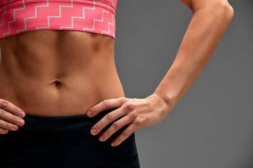 Croped close up body of fit woman wearing shorts and sport top showing slim beautiful stomach and abs in diet. Fitness and healthy lifestyle concept isolated on grey background