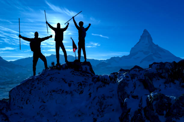 silhouette of two friends having achievement climbing up mountain to the peak together with background of sunrising