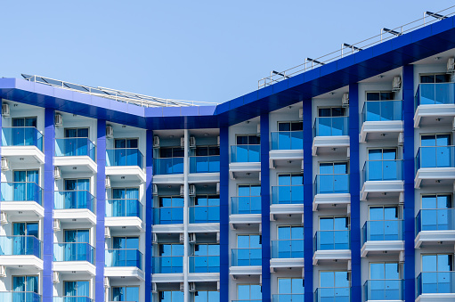 blue and white building with many balconies, large windows against the blue sky. Geometric shapes, minimalism