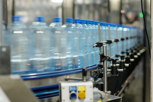 Part of factory robotic conveyor belt with row of moving capped plastic bottles containing filtered still or carbonated mineral water