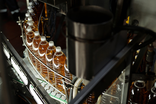 Row of packed plastic bottles with fizzy lemonade or other beverage moving along automated assembly line at plant or factory