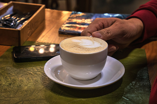 Cafe, hand holding a cappuccino cup with a delicious froth.