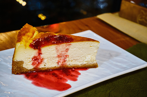 A delicious cheesecake on a white porcelain plate drizzled with raspberry jam.