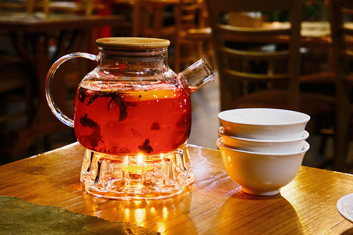 A glass teapot with berry tea, and porcelain cups nearby.