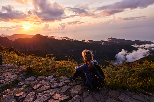 Back view of a female backpacker looking at view while having a break on a mountain at sunset. Copy space.