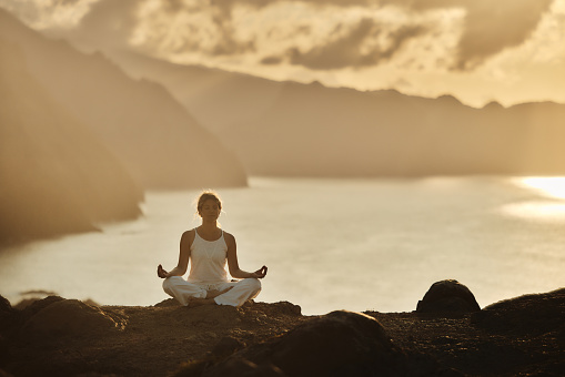 Athletic woman exercising Yoga in Lotus position on a mountain above the sea at sunset. Copy space.