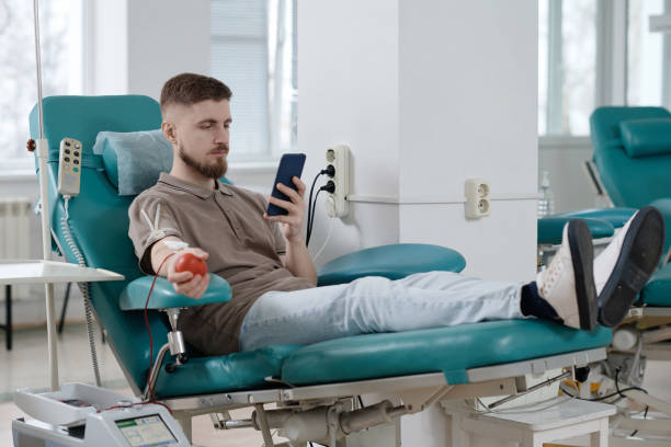 istock Young Caucasian Man Scrolling Smartphone During Blood Donation Process 1972078619
