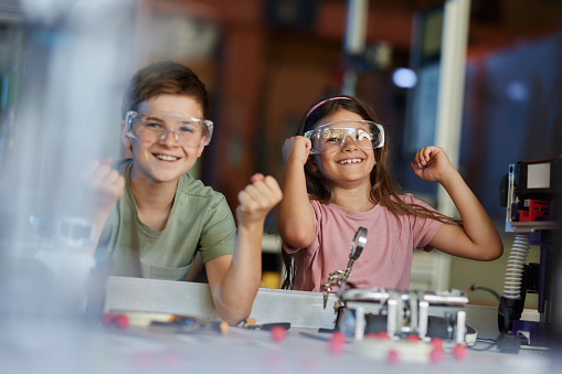 Happy little scientists celebrating their success while making robots during a science project in laboratory. Focus is on girl.