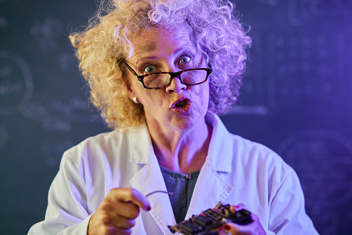 Portrait of crazy scientist trying to repair computer chip and looking at camera.