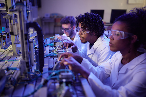 African American male scientist and his colleagues working on machinery in laboratory.