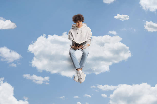 istock Casual young man sitting on a cloud and reading a book 1972094458