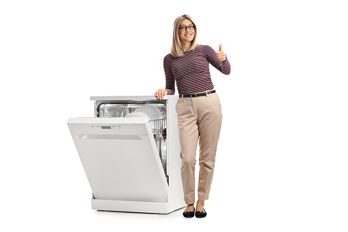 Woman with a half open white dishwasher gesturing thumbs up isolated on white background