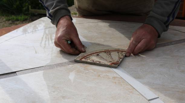 male hands lay out a square tile with a pattern in the middle of a mosaic made from large parts of tiles to create a decorative surface for furniture, the work of a tiler decorating products