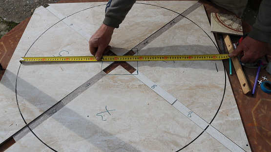 measuring the width of a drawn circle on a tiled surface of a craft product with a ruler, a craftsman measures the distance when making furniture, close-up
