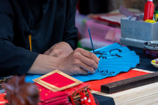 Selective focus of hand of Vietnamese scholar writes calligraphy at lunar new year. Calligraphy festival is a popular tradition during Tet holiday. Text in photo mean Happy New Year and Peace.