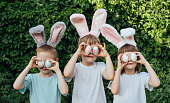 Smiling children wearing a headband with bunny ears found Easter eggs in the garden and brought them to their eyes