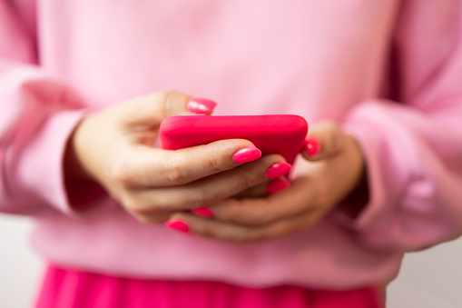 Close-up woman with pink manicure holding in hand and using mobile phone