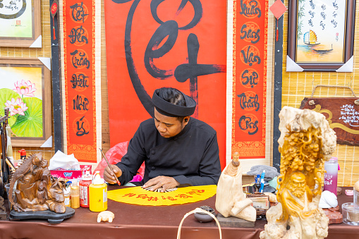 Ho Chi Minh city, Vietnam - 30 Jan 2024: Vietnamese scholar writes calligraphy at lunar new year. Calligraphy festival is a popular tradition during Tet holiday.