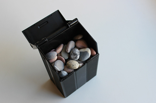 Black container mockup filled with colored pebbles on white stock photo to illustrate the theme of construction