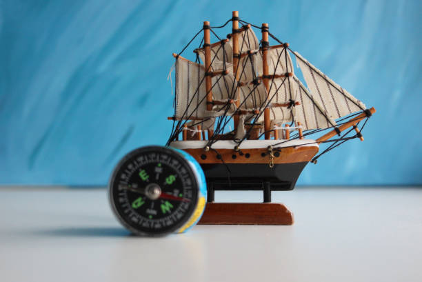 istock Wooden Sailing Ship Model And Vintage Compass On White Surface Over Blue Backdrop 1972168348