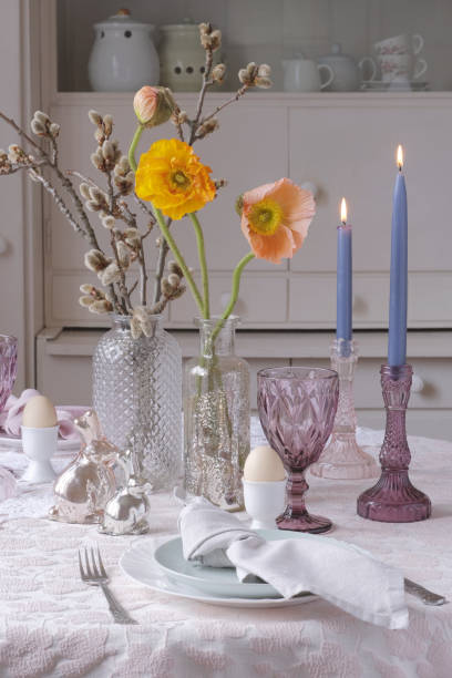istock Easter table decoration: poppies and flowering aspen branches in vases, rabbit figurines, candles in crystal candlesticks. Fragment. Orange and salmon poppies, blue candles, figurines made of mercury glass, maroon glass glasses. Vertical 1972181293
