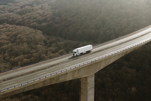 Aerial view of a semi truck on a tall highway viaduct in a mountain area