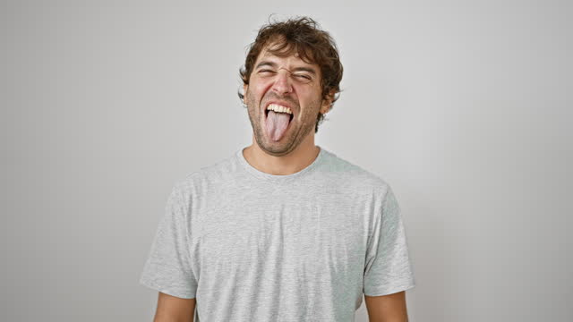 Handsome young man in casual t-shirt sticks his tongue out for a fun, positive expression of joy and happiness, isolated on white background.