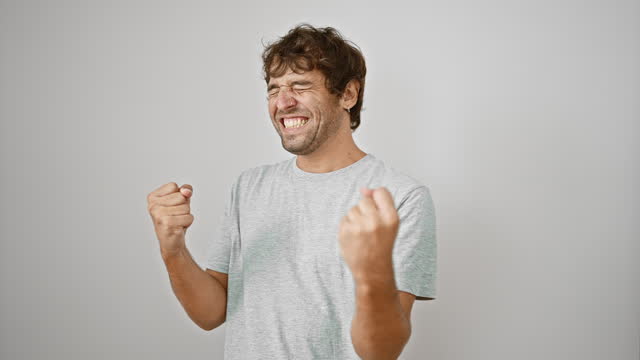 Excited young man in t-shirt celebrates win with joyful scream and victorious gesture on isolated white background
