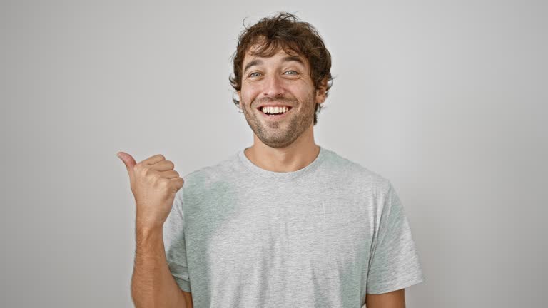 Cheerful young man in casual t-shirt, proudly pointing to the side with thumb up, flashing a beaming smile. perfect for product advertising on isolated white background.