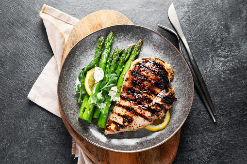 Grilled chicken breast and garnish of asparagus on a dark background. Top view.