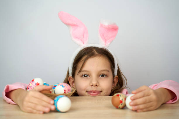 Funny happy child girl with easter eggs and bunny ears on white background with copy space.