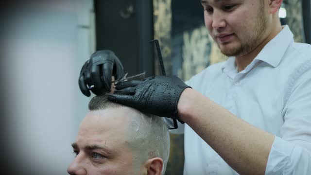 A hairdresser with a comb in his hands cuts a man's wet hair with scissors.