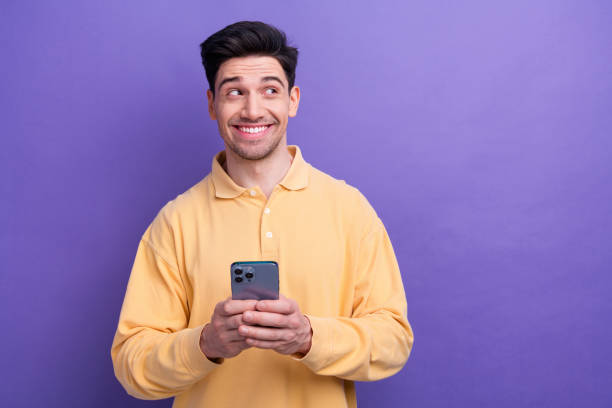 istock Photo of dreamy charming man dressed yellow shirt texting modern device looking empty space isolated purple color background 1972284694