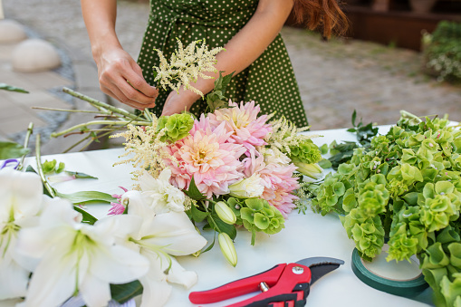Close-up of florist's hands as she carefully adds finishing touches to vibrant bouquet of pink dahlias and lush greenery.