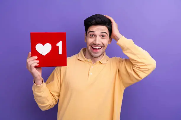 Photo of Photo of cheerful impressed guy wear yellow polo showing positive red heart cards isolated violet color background