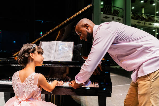 Teacher teaching child girl how to play piano on theater stage
