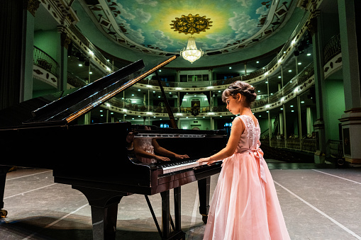 Child pianist girl playing piano at stage theater