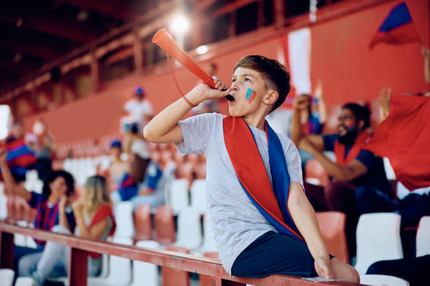 Kid blowing a vuvuzela during sports match at the stadium. Little boy celebrating victory of his sports team while blowing vuvuzela at the stadium. vuvuzela stock pictures, royalty-free photos & images