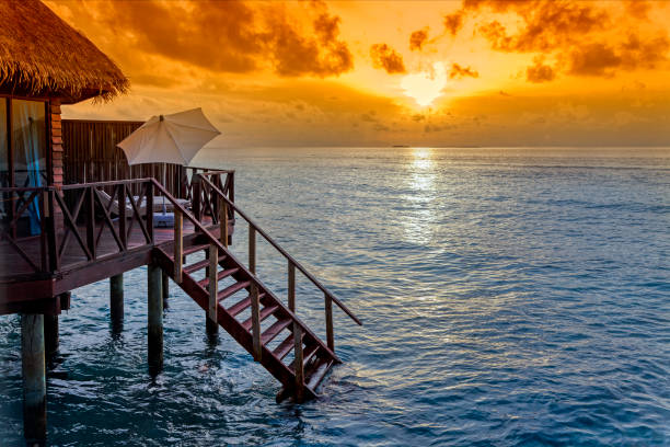 Sunrise or sunset over water bungalow on stilts with stairs into ocean on a tropical island, Maldives, Indian ocean