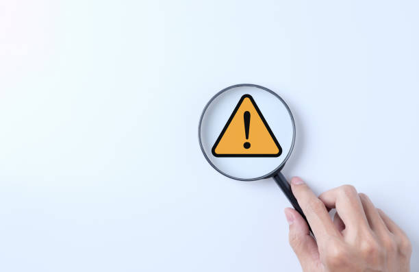 istock Warning alert system concept. Magnifying glass focused on yellow triangle warning sign. notification error and maintenance, cybercrime and virus, Malicious software, cybersecurity vulnerability, 1972341916