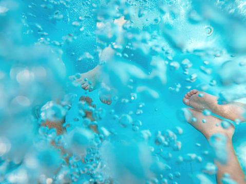 Family of three in hot tub, underwater shot of legs in bubbly pool water, selective focus