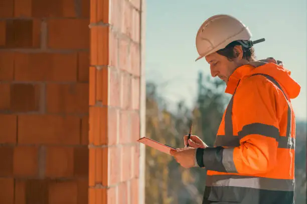 Construction engineer making notes and remarks during building site inspection, selective focus