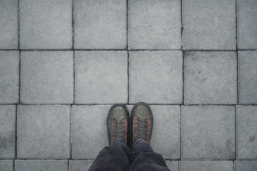 Man standing on the square shaped concrete pavement slabs, top view of dirty boots with copy space